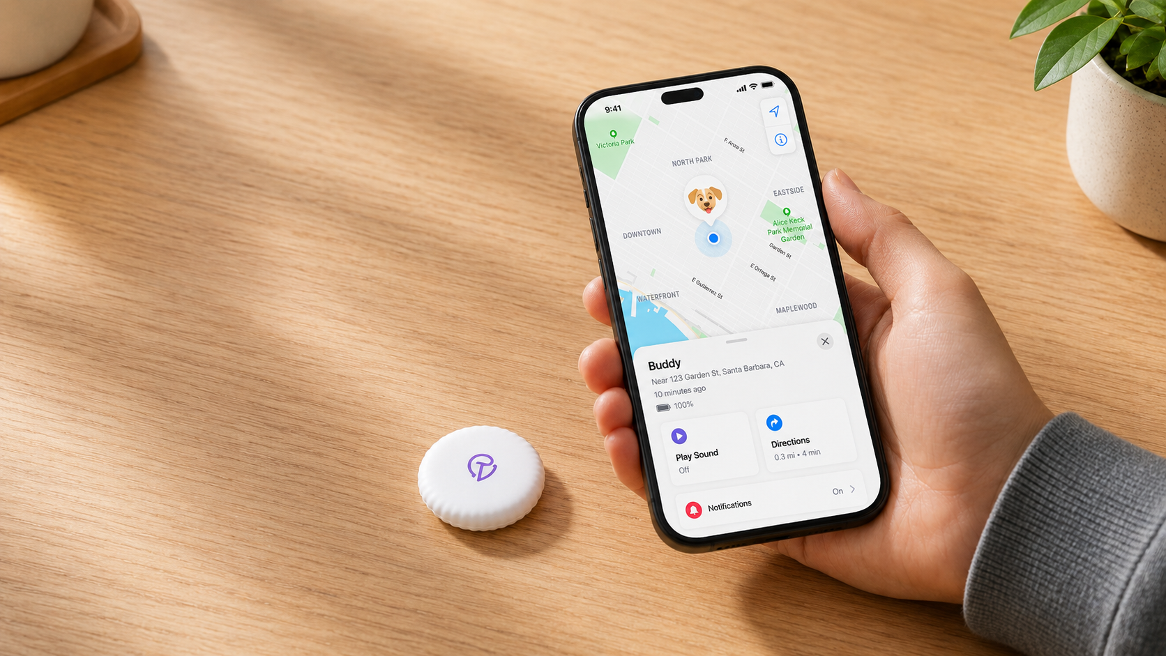 A hand holding an iPhone next to a Tracker Mist on a desk, mid-setup